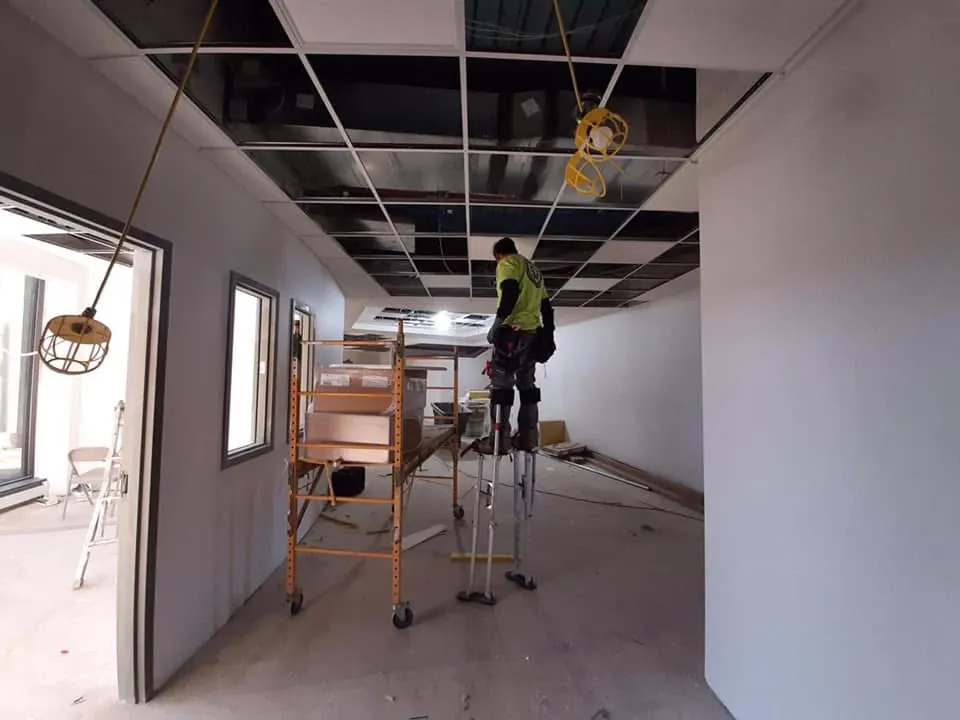 Skampy Acoustical crew member installing a suspended ceiling on stilts