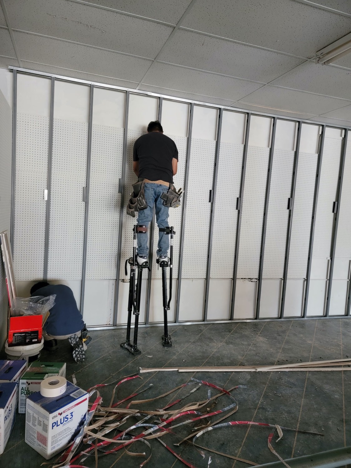 Skampy crew hanging and finishing drywall on stilts during a commercial build-out