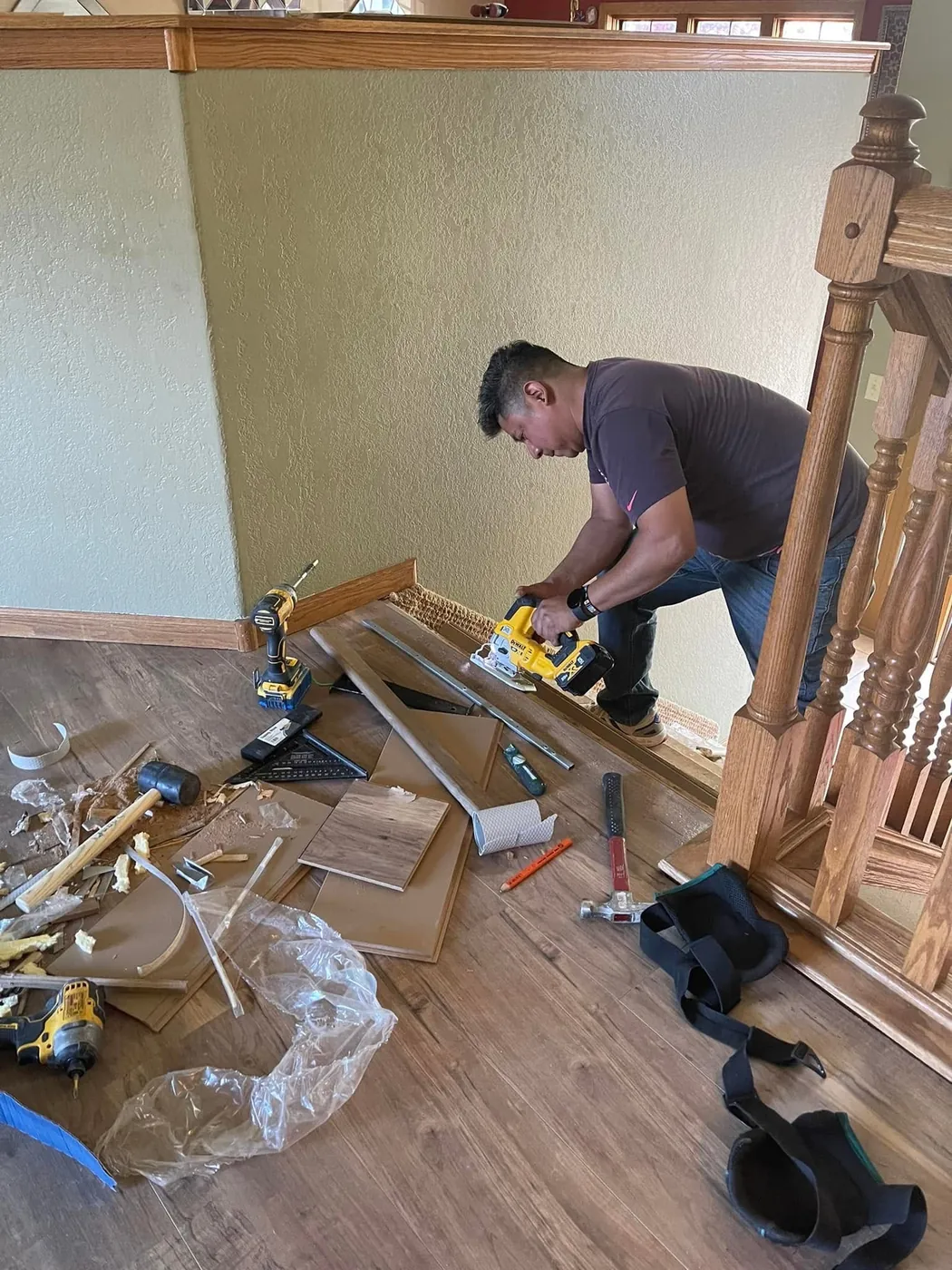 Skampy Construction installing vinyl plank flooring beside an oak staircase